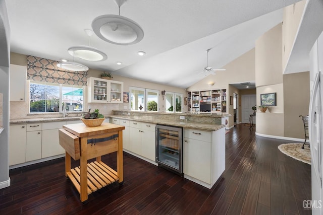 kitchen with wine cooler, dark wood-type flooring, vaulted ceiling, a sink, and a peninsula