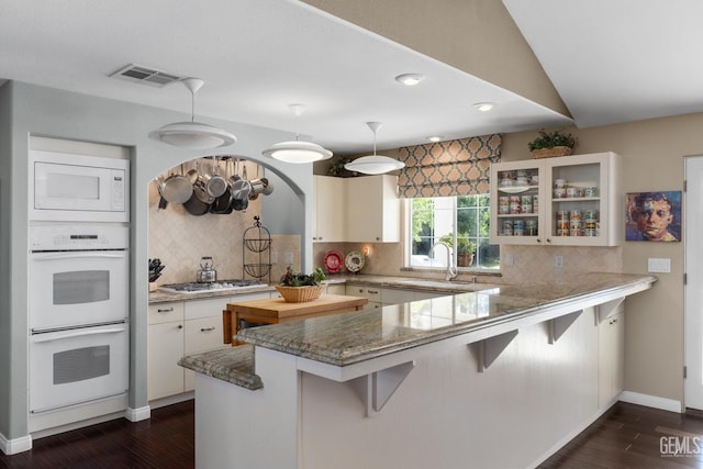 kitchen featuring a breakfast bar area, a peninsula, white appliances, a sink, and dark wood finished floors