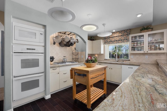 kitchen featuring white appliances, arched walkways, glass insert cabinets, dark wood-style flooring, and white cabinetry