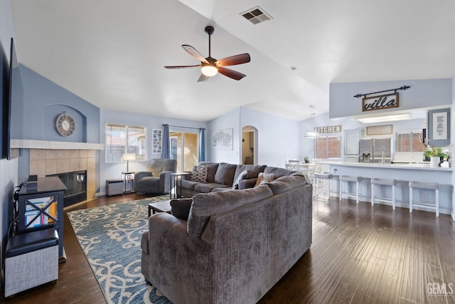 living area featuring arched walkways, lofted ceiling, a tile fireplace, wood finished floors, and visible vents