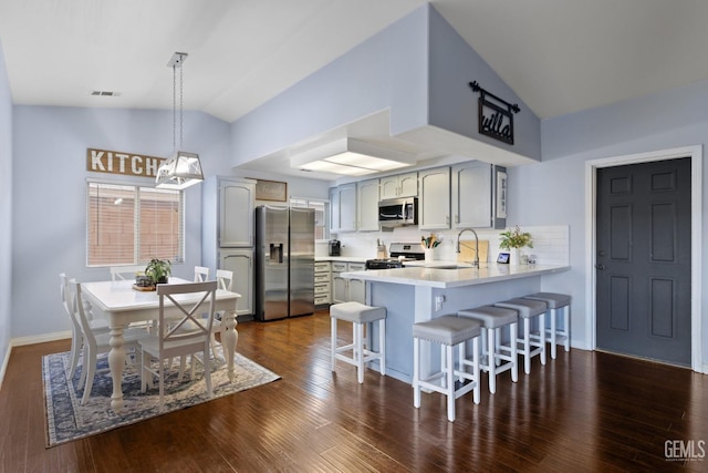 kitchen featuring lofted ceiling, a peninsula, visible vents, a kitchen breakfast bar, and appliances with stainless steel finishes