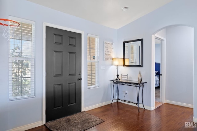 foyer entrance with arched walkways, plenty of natural light, baseboards, and wood finished floors