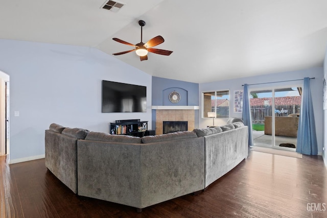 living area featuring lofted ceiling, ceiling fan, a tile fireplace, visible vents, and dark wood finished floors