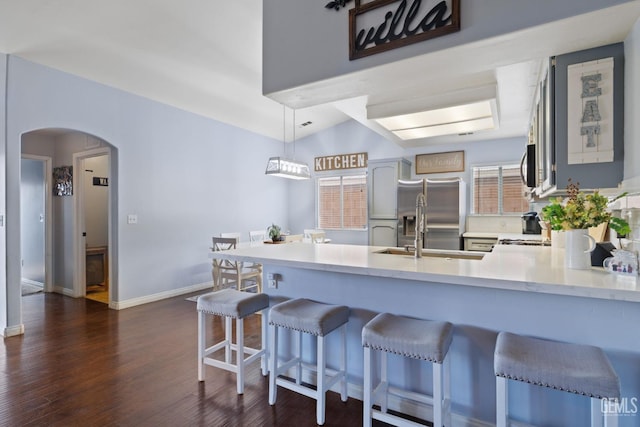 kitchen featuring arched walkways, a peninsula, dark wood-style flooring, light countertops, and appliances with stainless steel finishes