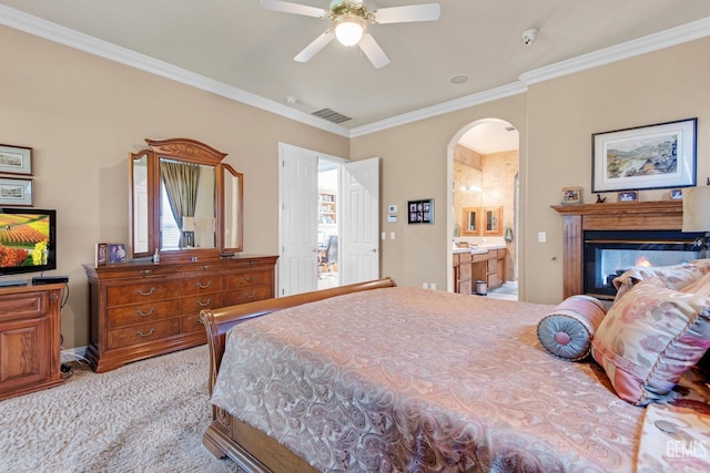 carpeted bedroom with visible vents, arched walkways, ensuite bath, ornamental molding, and a multi sided fireplace