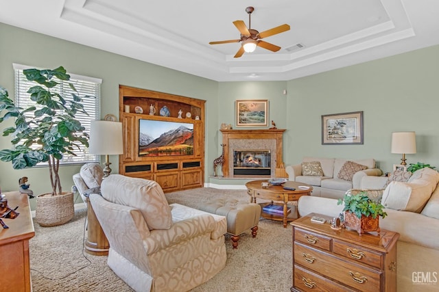 carpeted living room featuring visible vents, a raised ceiling, baseboards, ceiling fan, and a fireplace