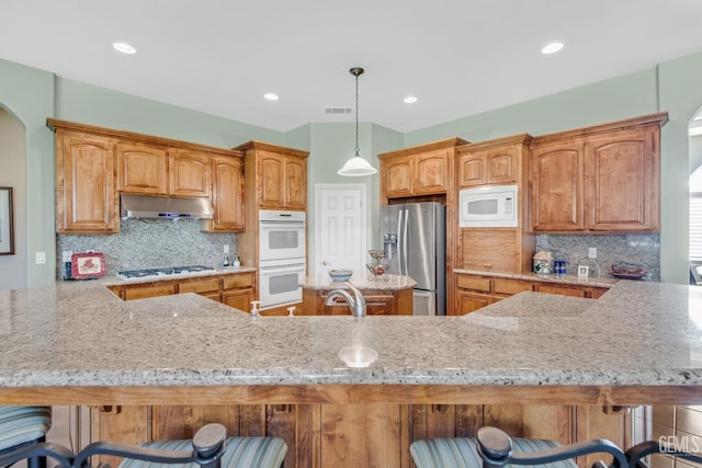 kitchen featuring light stone countertops, white appliances, under cabinet range hood, and a breakfast bar