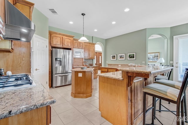 kitchen featuring light tile patterned floors, extractor fan, white appliances, visible vents, and a center island with sink