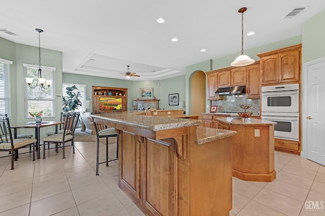 kitchen featuring double oven, visible vents, a center island with sink, and under cabinet range hood