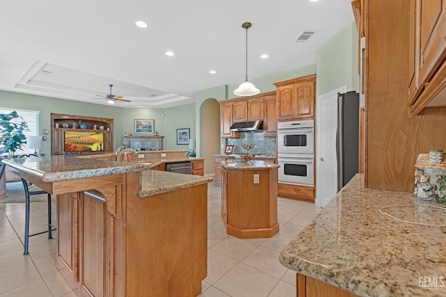 kitchen featuring a tray ceiling, arched walkways, light tile patterned floors, a spacious island, and stainless steel appliances