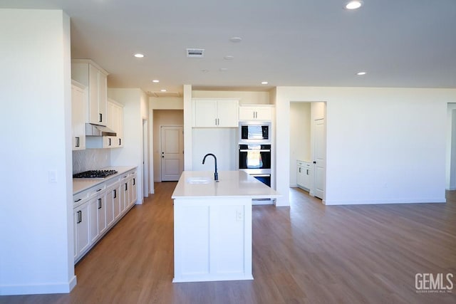 kitchen featuring built in microwave, stainless steel gas cooktop, white cabinetry, light hardwood / wood-style flooring, and an island with sink