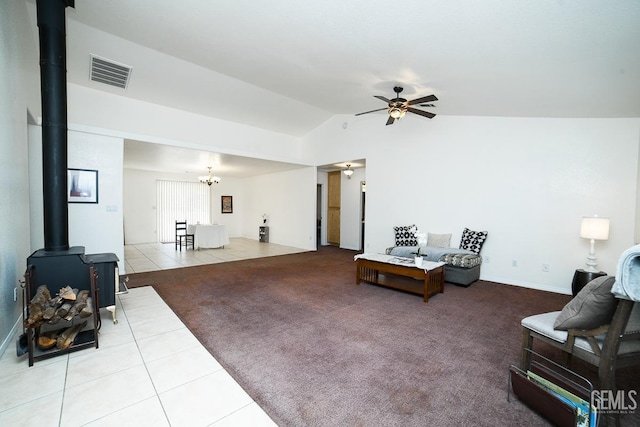 living room with a wood stove, ceiling fan with notable chandelier, light tile patterned floors, and vaulted ceiling