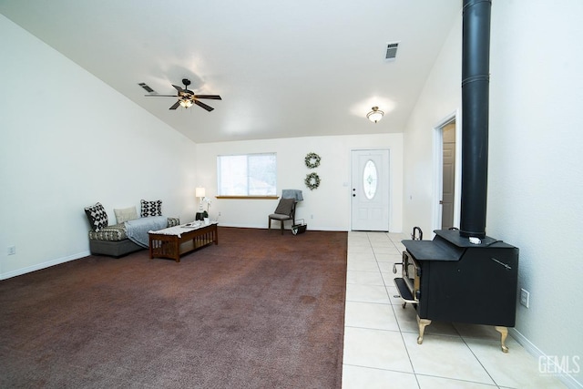 living room with ceiling fan, light tile patterned flooring, a wood stove, and lofted ceiling