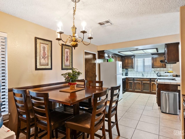 dining room with sink, a textured ceiling, light tile patterned floors, and a notable chandelier