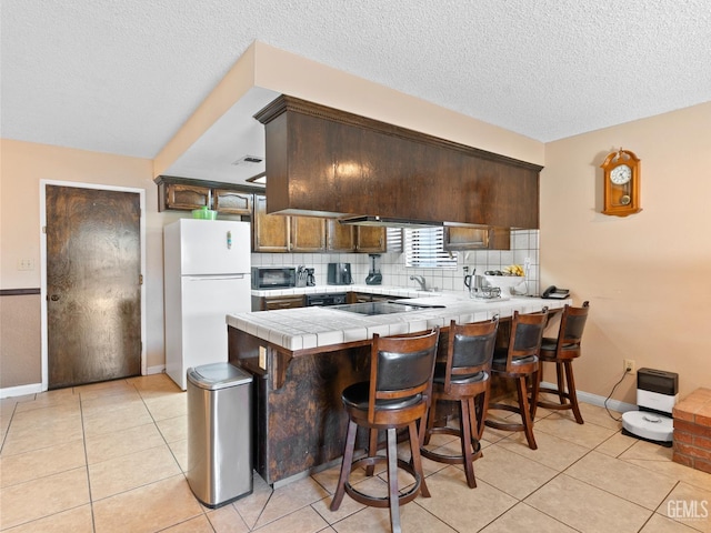 kitchen featuring a breakfast bar area, black appliances, kitchen peninsula, light tile patterned floors, and tile countertops