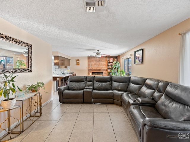 tiled living room featuring a brick fireplace, a textured ceiling, and ceiling fan