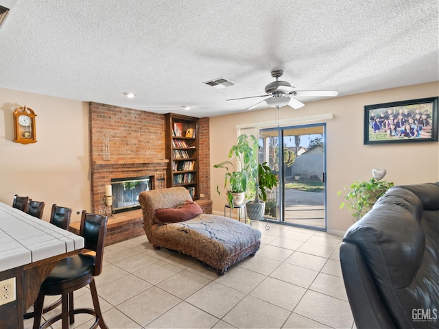 living room featuring a brick fireplace, a textured ceiling, built in shelves, and light tile patterned floors