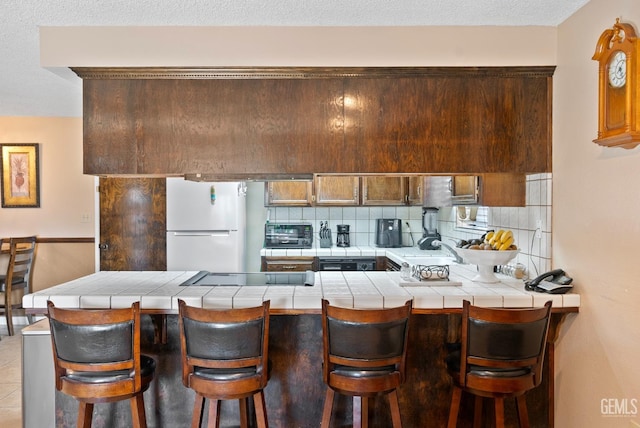 kitchen with kitchen peninsula, white refrigerator, tile countertops, and a breakfast bar