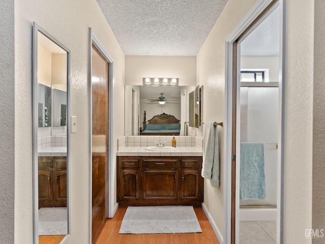 bathroom with a textured ceiling, hardwood / wood-style floors, decorative backsplash, a shower with door, and vanity