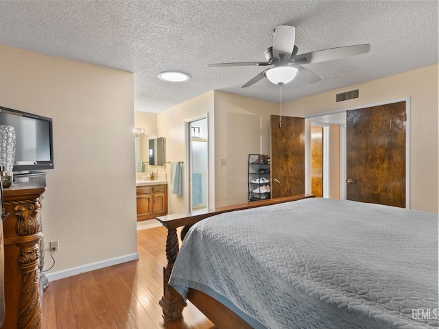 bedroom featuring ceiling fan, light wood-type flooring, ensuite bathroom, and a textured ceiling