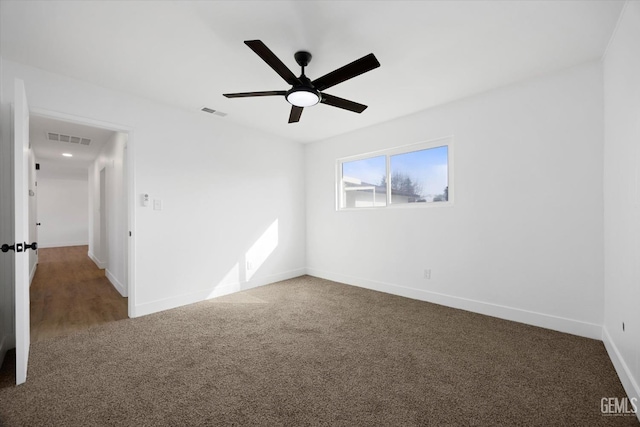 empty room featuring a ceiling fan, dark colored carpet, visible vents, and baseboards