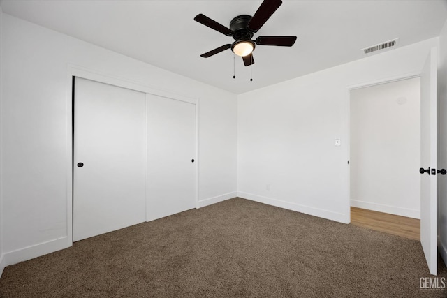 unfurnished bedroom featuring baseboards, visible vents, ceiling fan, dark carpet, and a closet