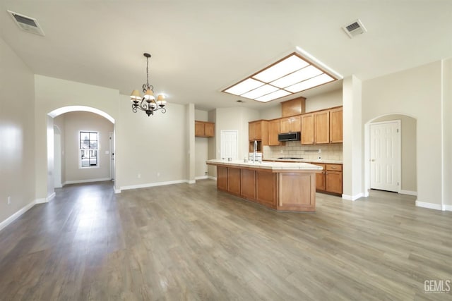 kitchen with an inviting chandelier, decorative light fixtures, an island with sink, hardwood / wood-style flooring, and backsplash