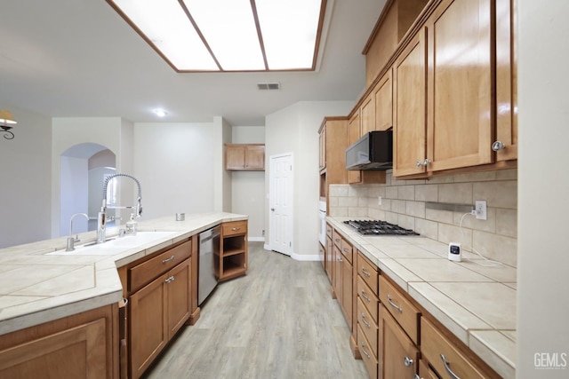 kitchen featuring sink, stainless steel appliances, tile counters, decorative backsplash, and light wood-type flooring