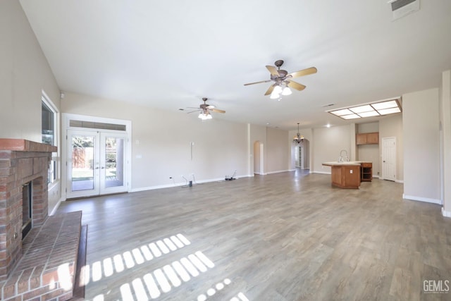 unfurnished living room featuring french doors, ceiling fan, dark wood-type flooring, and a brick fireplace