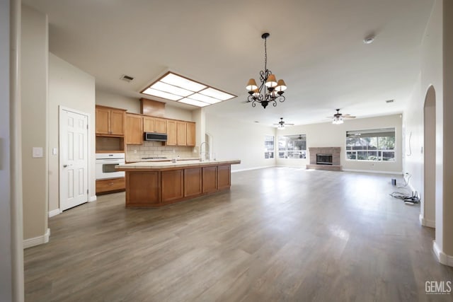 kitchen featuring white oven, hanging light fixtures, backsplash, wood-type flooring, and an island with sink