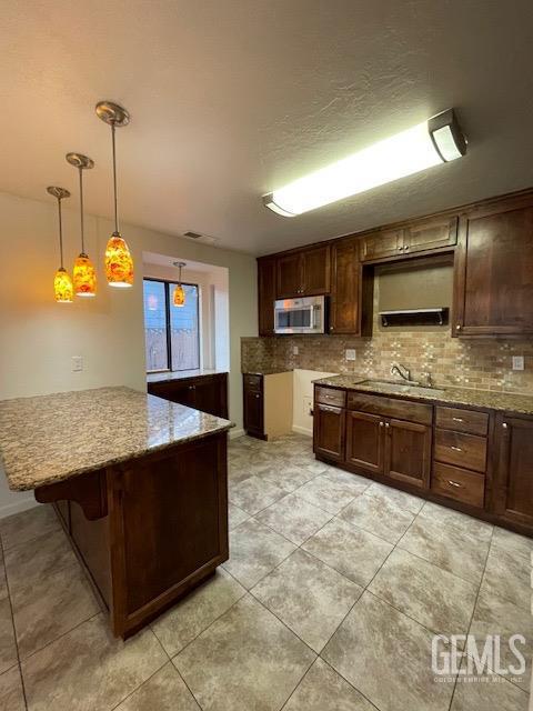 kitchen with stainless steel microwave, a peninsula, a sink, a kitchen bar, and backsplash