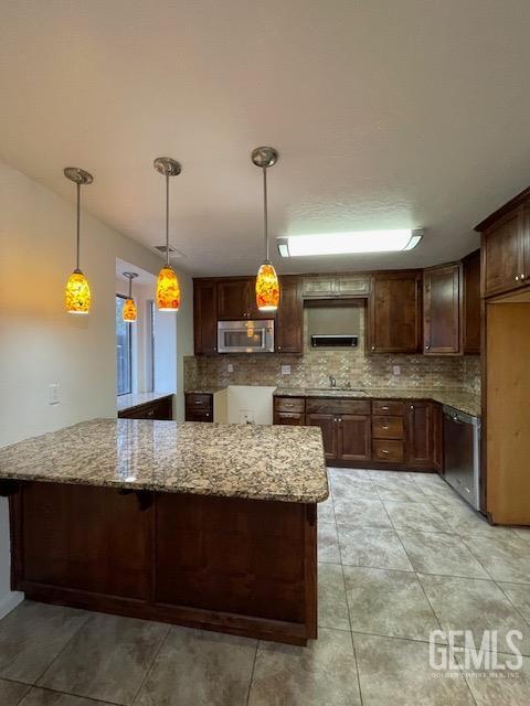 kitchen with light stone counters, stainless steel appliances, hanging light fixtures, backsplash, and a peninsula