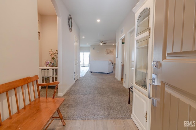 hallway featuring arched walkways, recessed lighting, baseboards, and light colored carpet