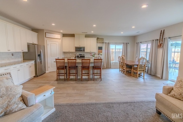 kitchen with tasteful backsplash, white cabinets, open floor plan, stainless steel appliances, and a kitchen bar