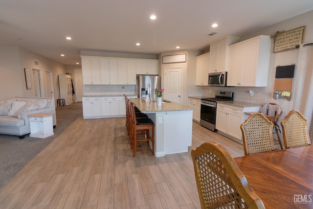 kitchen featuring appliances with stainless steel finishes, open floor plan, white cabinets, and a breakfast bar area