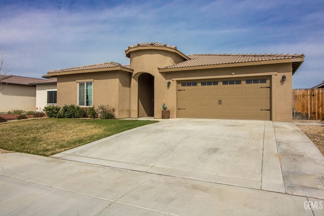 mediterranean / spanish house featuring a garage, driveway, stucco siding, fence, and a front yard