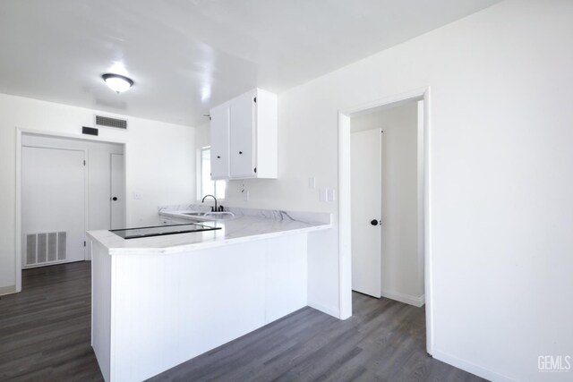 1312 Shattuck Ave, Bakersfield, CA 93305 - kitchen featuring dark wood-style flooring, light countertops, white cabinets, black electric stovetop, and a peninsula