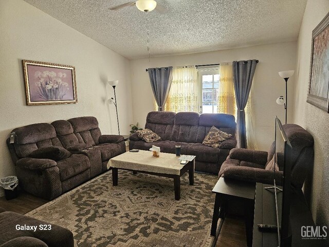 living room featuring ceiling fan, dark wood-type flooring, and a textured ceiling