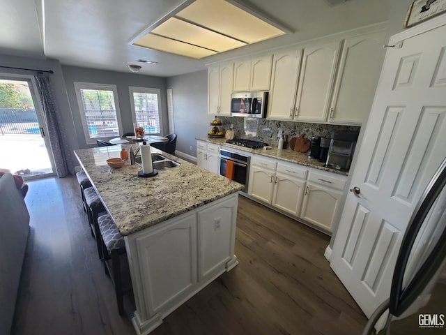 kitchen featuring stainless steel appliances, light stone countertops, a center island with sink, and white cabinetry