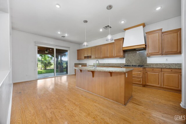 4702 Aviara Dr, Bakersfield, CA 93312 - kitchen featuring premium range hood, a sink, light wood finished floors, light stone countertops, and an island with sink