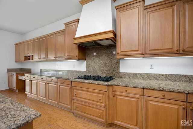 4702 Aviara Dr, Bakersfield, CA 93312 - kitchen with custom exhaust hood, black gas stovetop, light wood finished floors, decorative backsplash, and light stone countertops