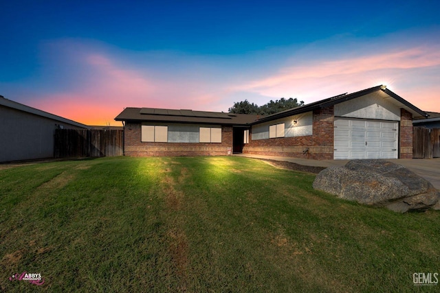 ranch-style house with a garage, a lawn, and solar panels