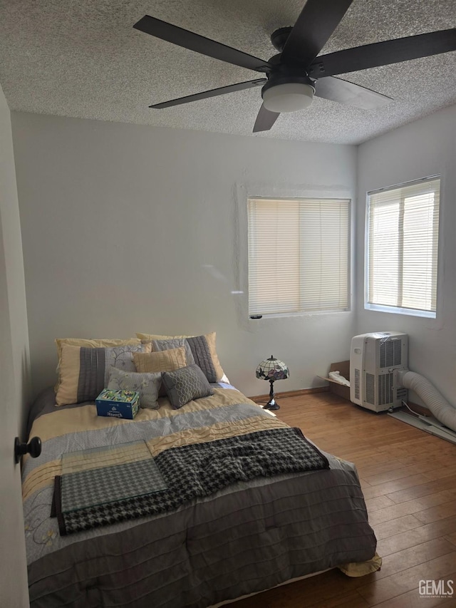 bedroom featuring ceiling fan, a wall mounted air conditioner, a textured ceiling, and hardwood / wood-style flooring