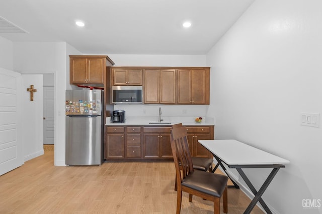 kitchen with a sink, light countertops, stainless steel appliances, and light wood-style flooring