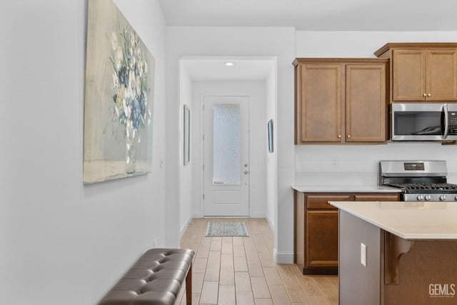 kitchen with light countertops, brown cabinetry, light wood-style flooring, stainless steel appliances, and baseboards