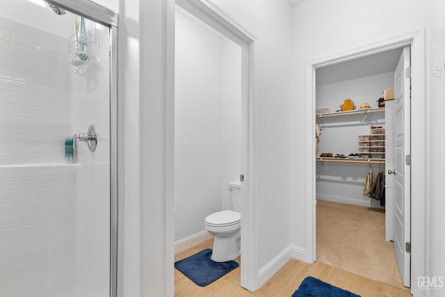 full bathroom featuring toilet, baseboards, wood finished floors, a spacious closet, and a stall shower