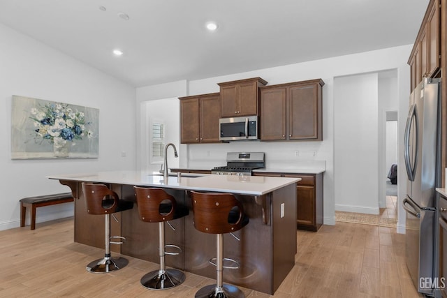 kitchen with light wood-style floors, baseboards, an island with sink, a sink, and stainless steel appliances