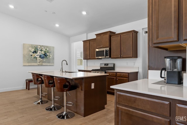 kitchen featuring a breakfast bar area, appliances with stainless steel finishes, a center island with sink, a sink, and light wood finished floors