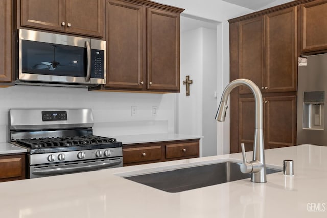 kitchen with dark brown cabinets, ceiling fan, light countertops, a sink, and stainless steel appliances