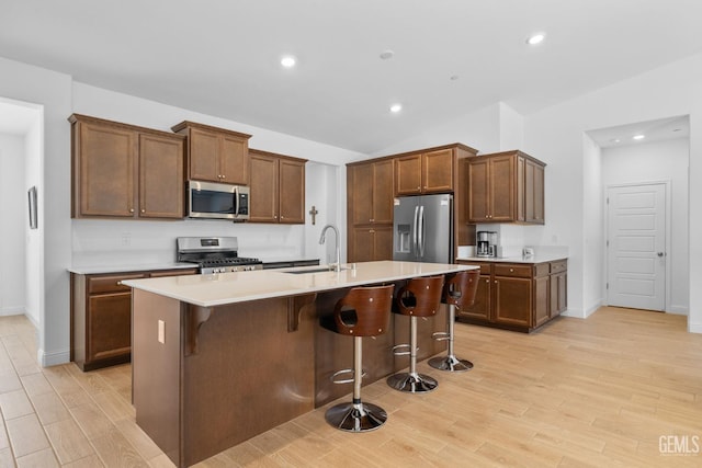 kitchen with a kitchen island with sink, a kitchen bar, light wood-type flooring, a sink, and stainless steel appliances